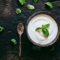 Greek yogurt or sour cream with a mint leaf  in a wooden bowl on dark table top view. Healthy food nutrition.